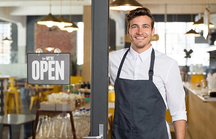 Man in apron next to 'Open' sign