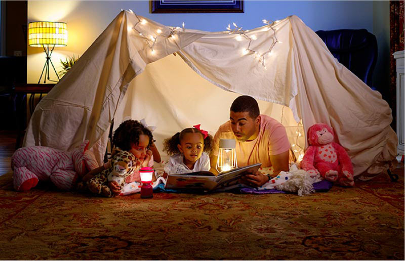 Dad reading to daughters in blanket fort